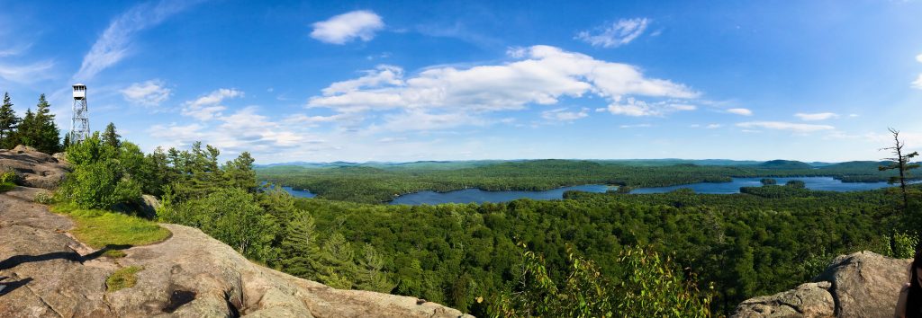 Vantage point from Bald Mountain. Scenic views include a tower to the left, the green pine trees, and part of the lake. One of the many things to experience in the Adirondacks.