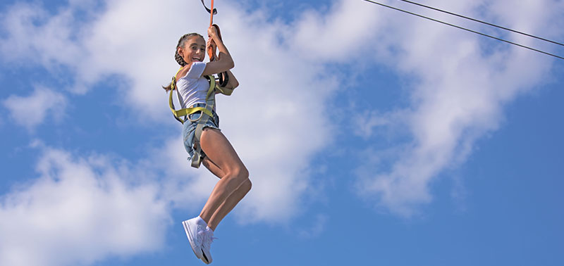 A guest smiling while taking a ride on the zip-line at Calypso's Cove.